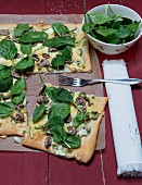 Tarte flambée with mushrooms, spinach and spring onions a piece of baking paper on a red wooden surface
