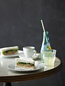 Thunfisch-Rucola-Tramezzini, Cappuccino und Limonade auf Bistrotisch