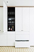 White, floor-to-ceiling built-in cupboard with drawers and open cupboard door in a kitchen