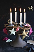 A unique Advent wreath on a cake stand decorated with paper stars, a golden garland and four burning candles
