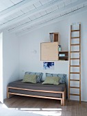 Wooden ladder next to pull-out bed in corner below wall-mounted cupboard modules
