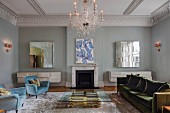 Glass coffee table with brass base, pale blue retro armchairs and green velvet sofa in front of fireplace in grand, eclectic living room