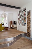 Eclectic living area on platform and firewood stacked in vertical niche next to white fitted shelves