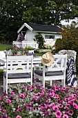 weiße Holzstühle und Tisch auf Terrasse, im Hintergrund Gartenhäuschen