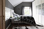 Blick auf Boxspringbett vor grau gestrichener Holzwand in ländlichem Schlafzimmer