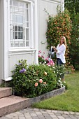 Frau beim Blumengiessen vor traditionellem Landhaus