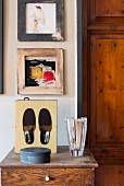 Glass vase and black slippers in box on top of cabinet below pictures on wall