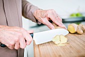 An older woman slicing ginger on a wooden chopping board