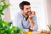 Mann stützt sich auf Küchentheke und isst Apfel