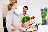 Paar in der Küche: Mann mit Gemüsekiste, Frau beim Schneiden von Obst