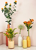 Blumen in mit Farbe gestalteten Flaschen und Gläsern