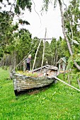 Little girl climbing on rustic sailing dinghy used as sandpit in garden