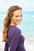 Junge blonde Frau in violettem Langarmpulli am Strand