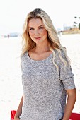 A young blonde woman wearing on a beach wearing a knitted mottled grey top