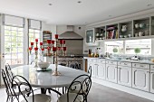 Metal dining chairs around silver candelabras on white table in front of country-house kitchen counter