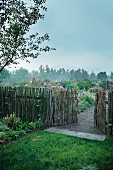 Knüppelzaun mit offenem Tor und Blick in Garten
