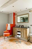 Double country-house-style washstand next to modern, orange, masonry toilet screen and upholstered stool