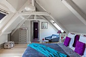 Wooden beams and colourful bed linen in attic bedroom