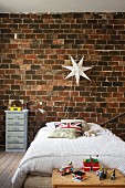 Bed below star-shaped lamp on rustic brick wall in boy's bedroom