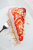 A slice of strawberry yoghurt cake on a biscuit base with fresh strawberries and white chocolate