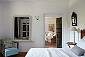 Ländliches Schlafzimmer mit blauem Sessel neben Wandspiegel und offener Verbindungstür zum Wohnbereich