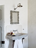 Waschbecken aus Stein mit Wandarmatur, Wandspiegel und Wandleuchte in schlichtem Bad