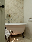 Freistehende Badewanne mit Klauenfüssen, davor Teelichter auf Steinfliesenboden