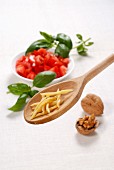 Strozzapreti on a wooden spoon with tomatoes, basil and walnuts