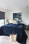 Doppelbett mit dunkelblauer Tagesdecke, seitlich minimalistische Pendelleuchten