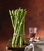 A bundle of green asparagus on a wooden table with wine and garlic