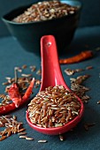 Roter Reis auf Keramiklöffel und Chilischoten auf Schieferuntergrund