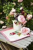 Romantischer Gartenblumenstrauss in Porzellankanne auf gestricktem Deckchen mit Rosenmotiv