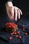 A hand taking mini redcurrant tomatoes from a copper pan