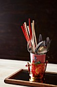 Chopsticks and cutlery in vintage beakers in pot with Oriental pattern