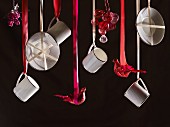 Schwebende Tassen und Untertassen, dazwischen Dekofiguren an roten Schleifenbändern