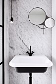 Washbasin with black fittings in front of marble wall with round mirrors