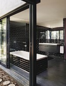 Bad mit schwarzen, glänzenden Wandfliesen, Badewanne und geöffneter Terrassenschiebetür