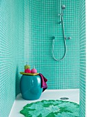Duschbereich mit türkisfarbenen Mosaikfliesen an Wand, bauchiger Schemel mit Badutensilien