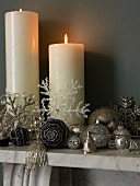 Burning white pillar candles and silver Christmas decorations on a mantelpiece