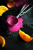 An ice cream scoop with melted berry sorbet and oranges