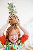 A little girl holding a fresh pineapple above her head
