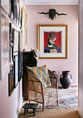 Wicker armchair, footstool and gallery of pictures on pink walls in foyer