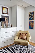 Comfortable retro armchair in front of white fitted cabinets and modern portraits