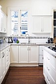 weiße Übereck-Landhausküche mit schwarz-weisser Bordüre unter Hängeschränkchen