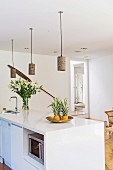 White kitchen island with pineapple and bouquet of lilies, above it DIY pendant lights made from lanterns