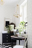 Console table below window and black chest of drawers in bathroom with white subway wall tiles