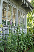 Blumenbeet vor traditionellem Wintergarten mit verzierter Holzfassade und Sprossenfenstern