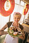 A blonde woman holding a selection of doughnuts on a plate