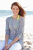 A young brunette woman on a beach wearing a grey top and white trousers