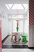 White table, green bench and shell chairs on black and white tiled floor under skylight